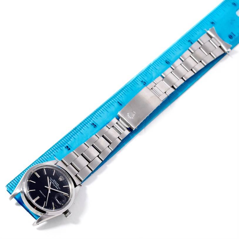 The image shows a top-down view of a Rolex Air-King 5700 Men's Stainless Steel Black Dial 5700 Men's Stainless Steel Black Dial watch, including its dial, bracelet, and clasp, next to a ruler for scale.