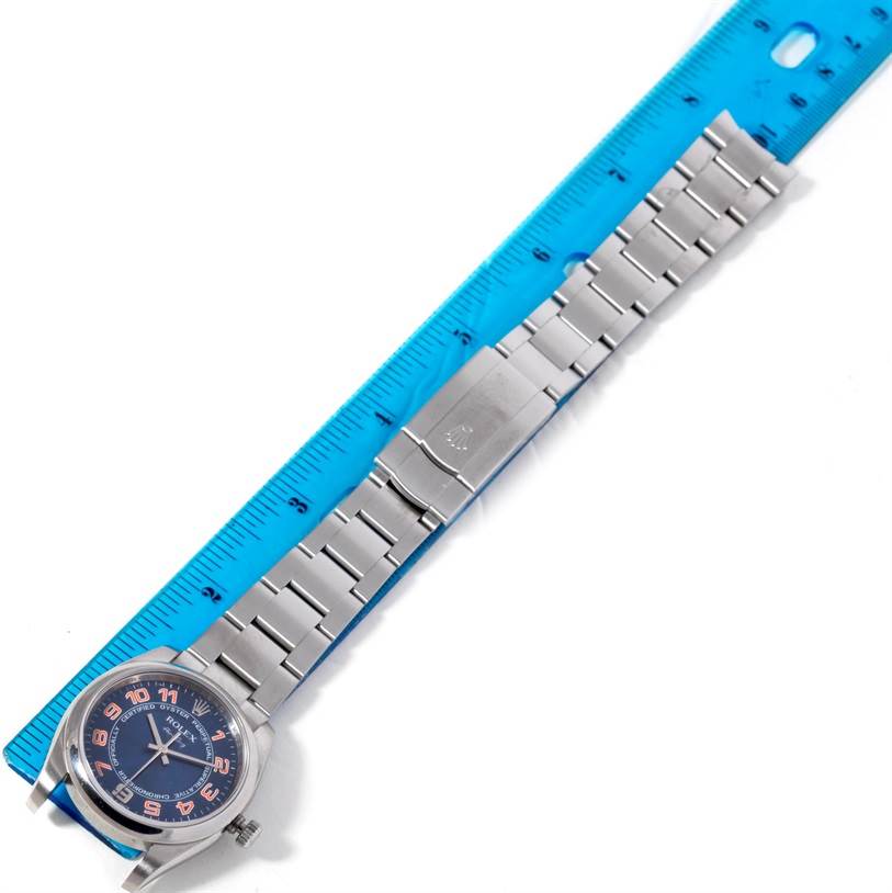 The image shows a top-down view of a Rolex Air-King 114200 Men's Stainless Steel Blue Dial 114200 Men's Stainless Steel Blue Dial watch and part of its bracelet placed next to a blue ruler.
