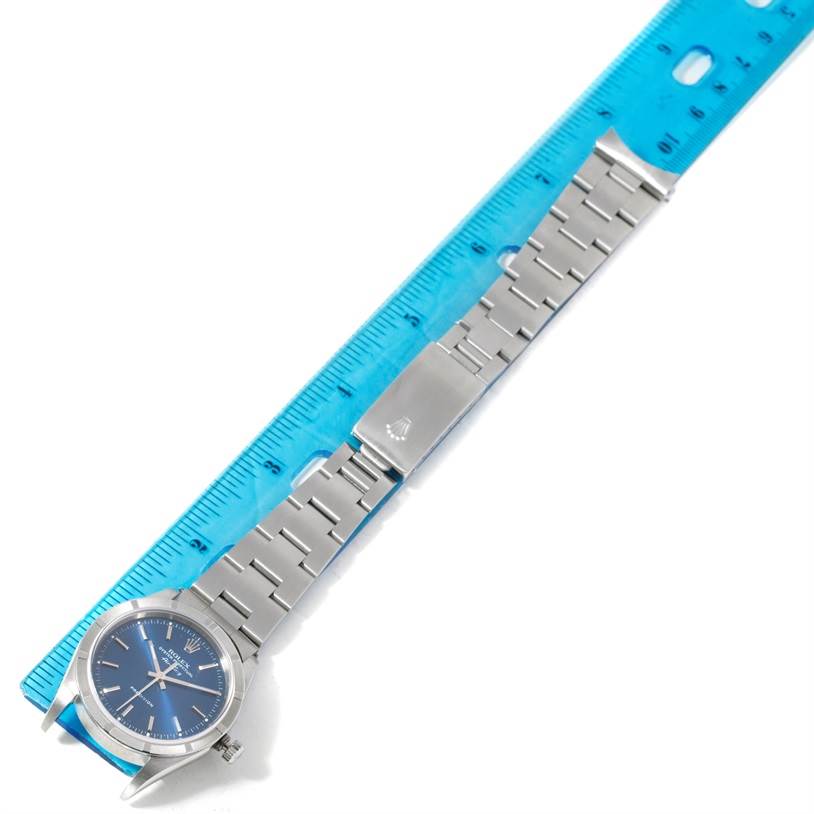 The Rolex Air-King 14010 Men's Stainless Steel Blue Dial 14010 Men's Stainless Steel Blue Dial watch is displayed horizontally with its blue dial and metal bracelet laid next to a blue ruler.