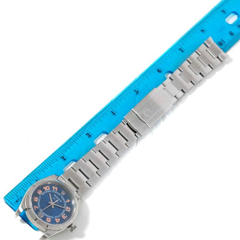 The Rolex Air-King 114210 Men's Stainless Steel Blue Dial 114210 Men's Stainless Steel Blue Dial watch is shown from a top-down angle, displaying the dial, bracelet, and clasp, beside a blue ruler for scale.