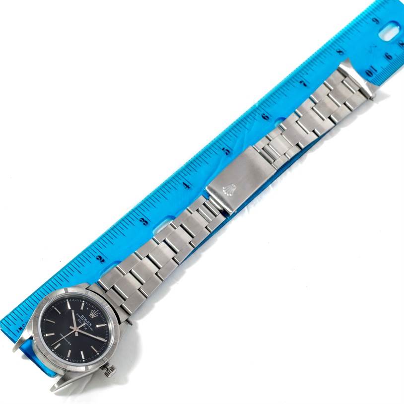 The image shows an overhead view of a Rolex Air-King 14010 Men's Stainless Steel Black Dial 14010 Men's Stainless Steel Black Dial watch with its metal bracelet placed next to a blue ruler.
