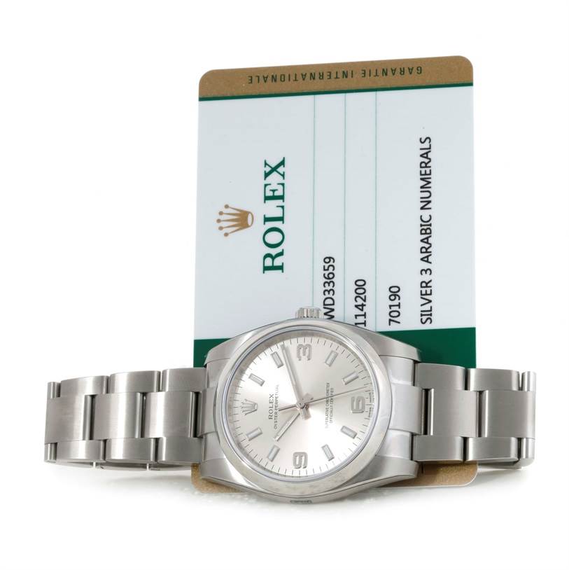 The image shows a Rolex Air-King 114200 Men's Stainless Steel Silver Dial 114200 Men's Stainless Steel Silver Dial watch laid flat with its bracelet fully extended and a guarantee card placed behind it.