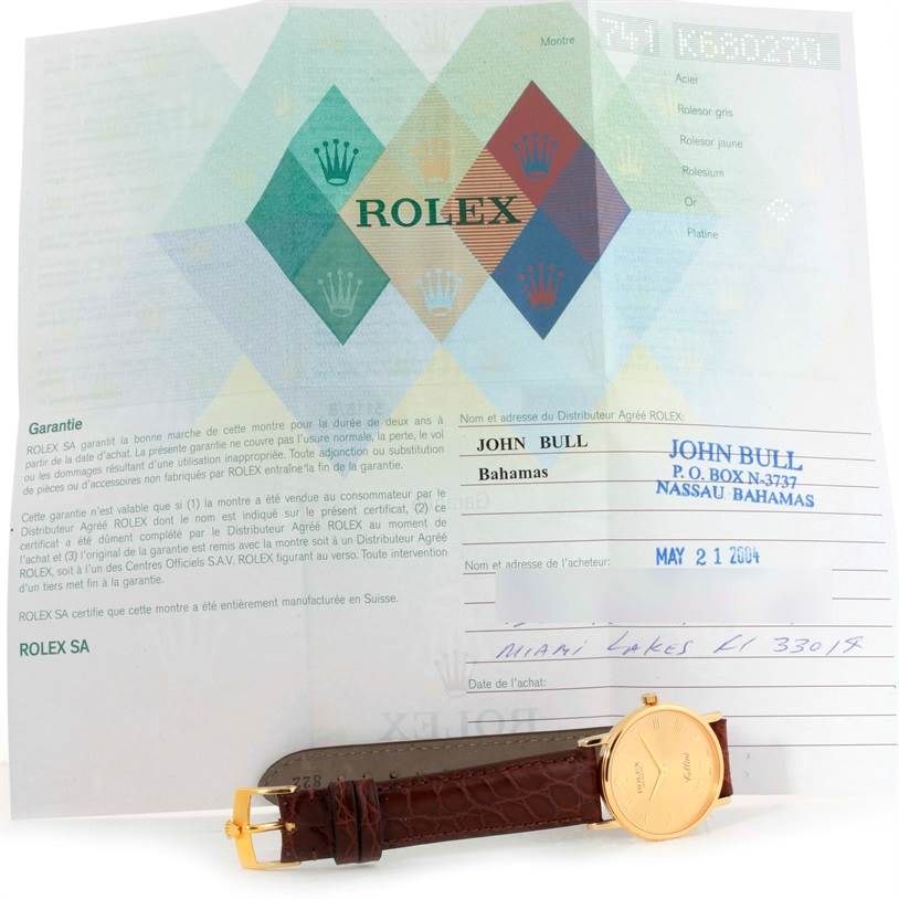 The image shows a Rolex Cellini 5115 Men
s Yellow Gold Champagne Dial 5115 Men
s Yellow Gold Champagne Dial watch with a gold case and brown leather strap, presented alongside its guarantee paperwork.