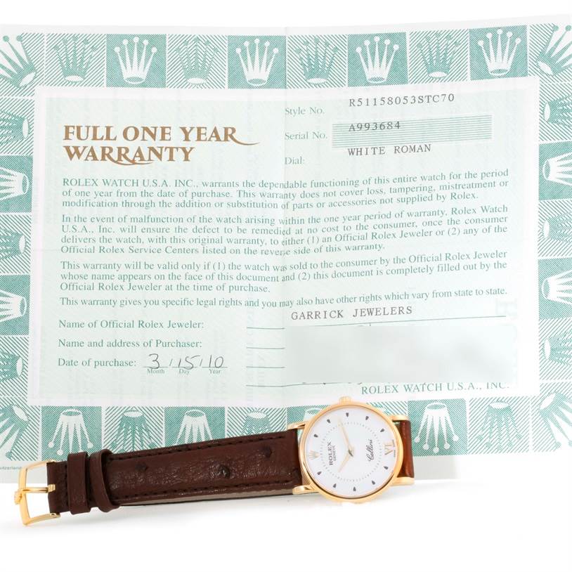 The Rolex Cellini 5115 Men
s Yellow Gold Silver Dial 5115 Men
s Yellow Gold Silver Dial watch is shown from a top-down angle, alongside its warranty card.