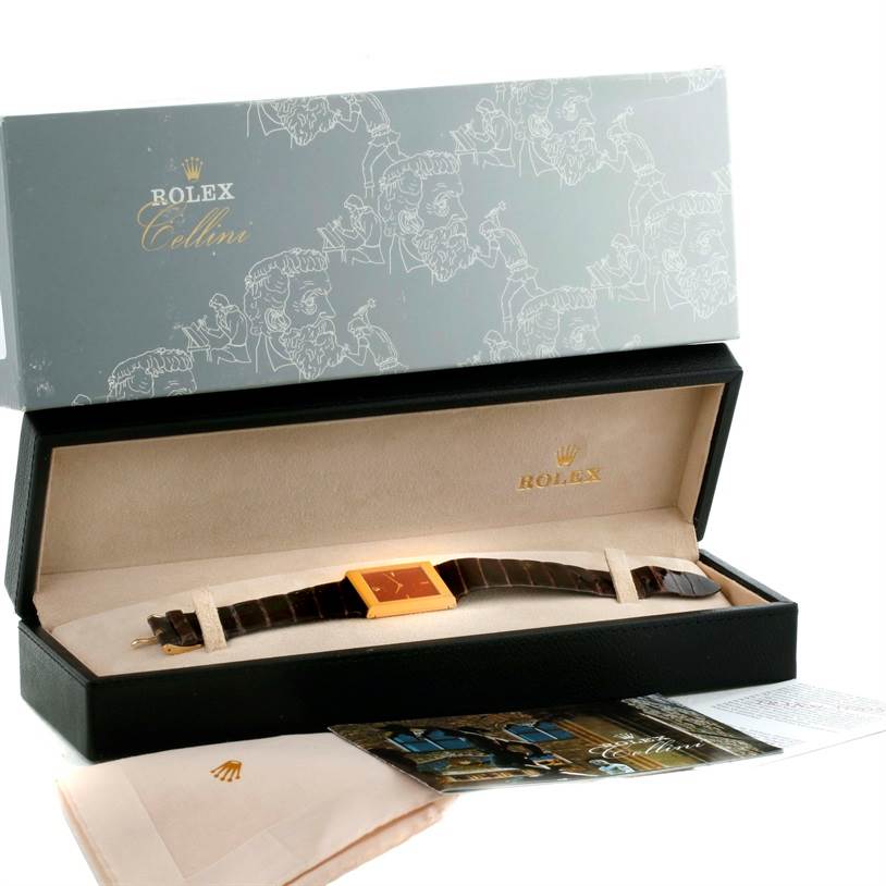 The Rolex Cellini 4127 Men
s Yellow Gold Champagne Dial 4127 Men
s Yellow Gold Champagne Dial watch is shown from the top angle, inside its open box with its strap fully extended and some accompanying documents visible.