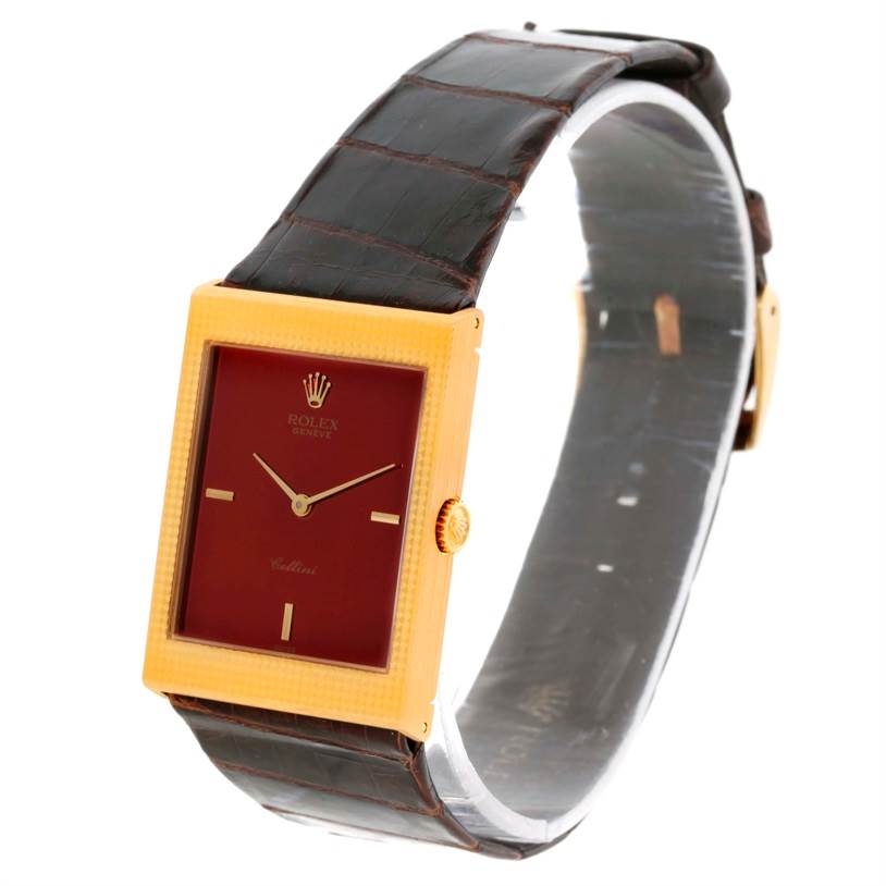 The Rolex Cellini 4127 Men
s Yellow Gold Champagne Dial 4127 Men
s Yellow Gold Champagne Dial watch is shown at a three-quarter angle, highlighting its rectangular gold case, red dial, and dark leather strap.