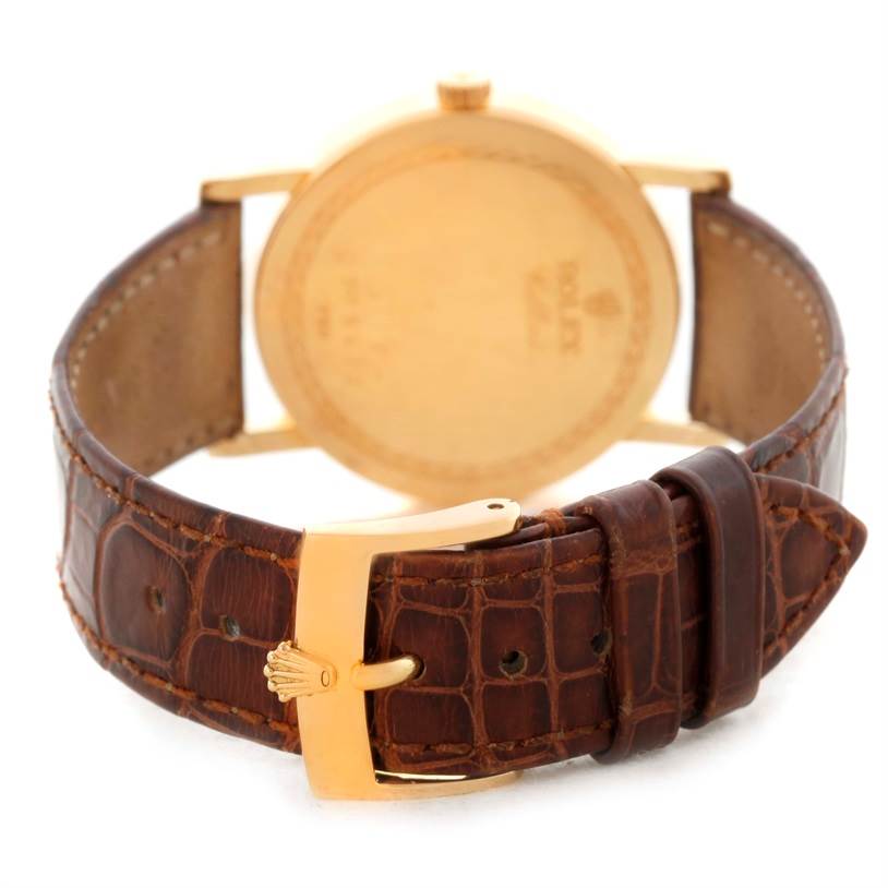 The image shows the back view of a Rolex Cellini 5115 Men
s Yellow Gold Champagne Dial 5115 Men
s Yellow Gold Champagne Dial watch, highlighting its gold case and brown leather strap with the Rolex logo on the buckle.