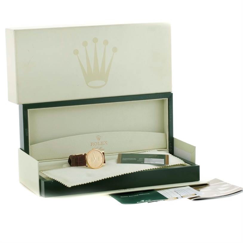 The image shows a Rolex Cellini 5115 Men
s Yellow Gold Champagne Dial 5115 Men
s Yellow Gold Champagne Dial watch in an open presentation box with accompanying papers and a cleaning cloth.