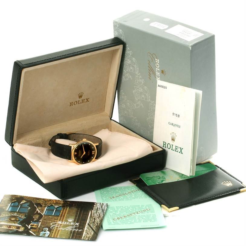 The Rolex Cellini 5115 Yellow Gold Black Dial 5115 Yellow Gold Black Dial watch is shown in an open box with additional accessories including manuals, booklets, and an outer box.