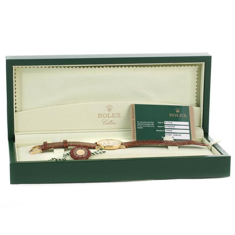 The image shows a Rolex Cellini 5115 Men
s Yellow Gold Beige Dial 5115 Men
s Yellow Gold Beige Dial watch in its box with a warranty card and a tag.