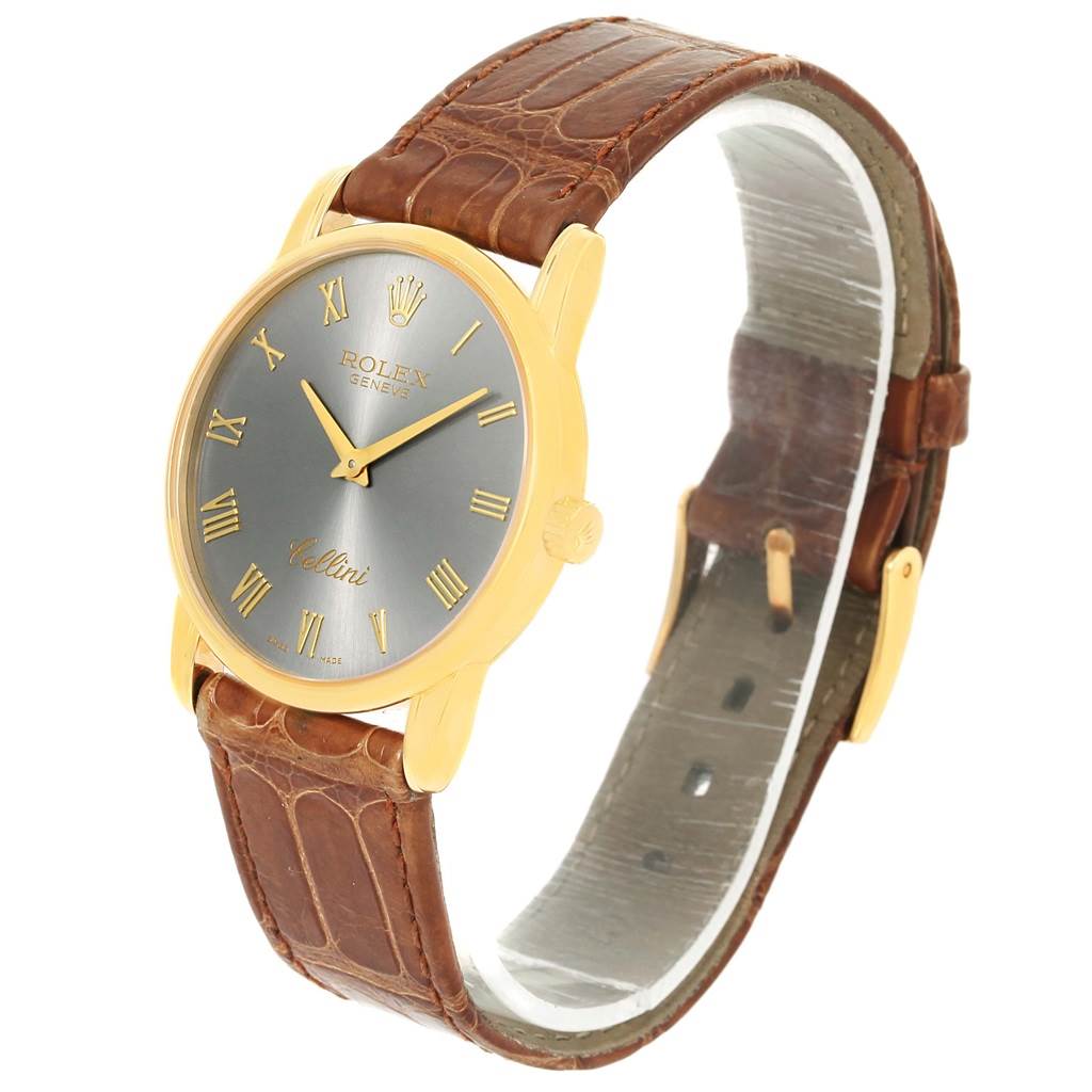 The Rolex Cellini 5116 Men's Yellow Gold Grey Dial 5116 Men's Yellow Gold Grey Dial watch is shown at a three-quarter angle, highlighting its gold case, gray dial with gold Roman numerals, and brown leather strap.