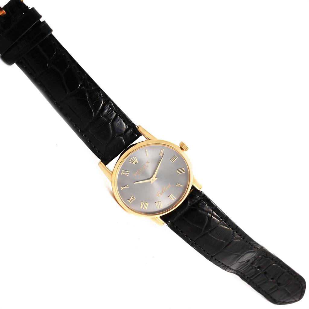 The image shows a Rolex Cellini 5116 Yellow Gold Grey Dial 5116 Yellow Gold Grey Dial watch from a top-down angle, depicting its black strap, gold case, and analog dial.