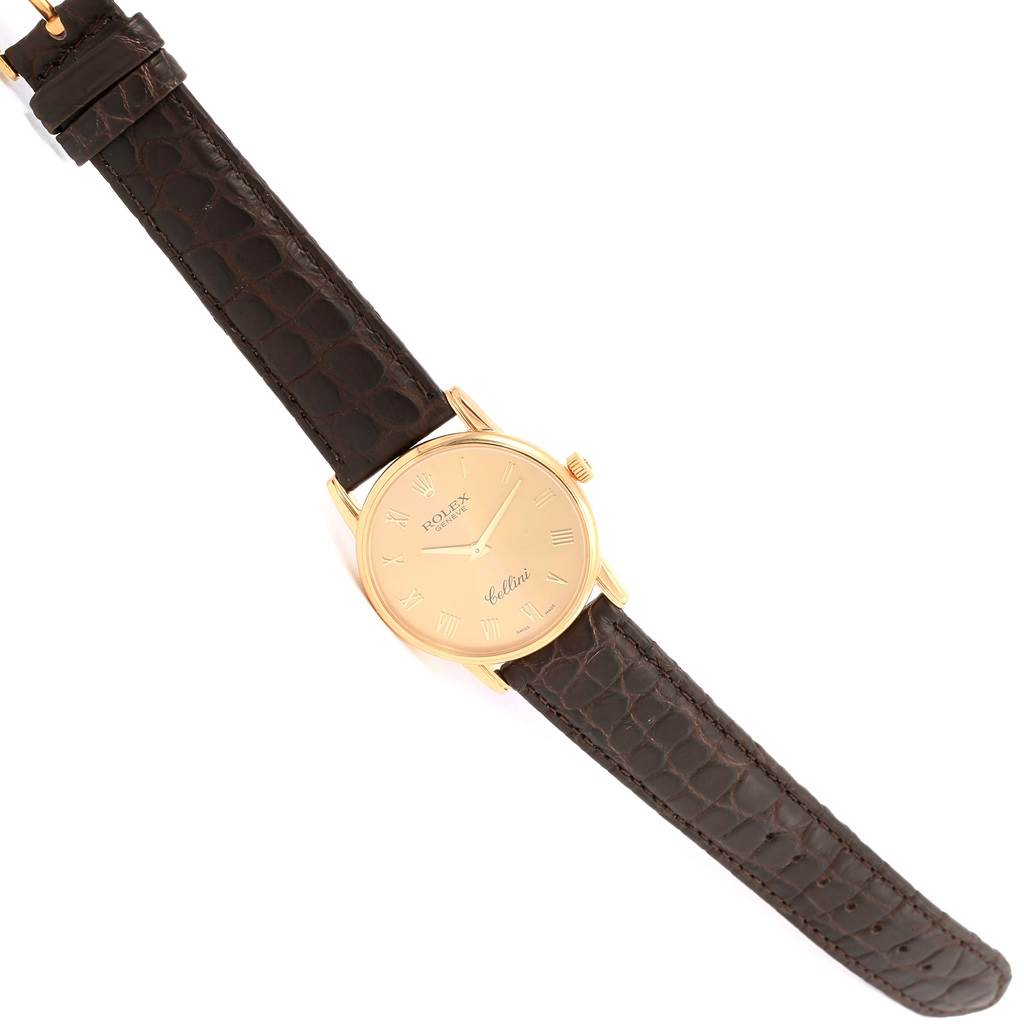 The Rolex Cellini 5116 Men's Yellow Gold Champagne Dial 5116 Men's Yellow Gold Champagne Dial watch is shown from a top-down angle, displaying its gold case, dial, and brown leather strap.