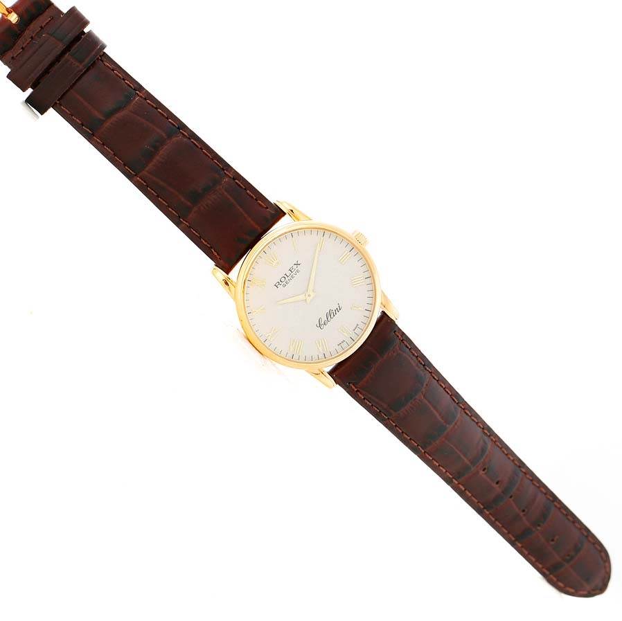 The Rolex Cellini 5116 Men's Yellow Gold Beige Dial 5116 Men's Yellow Gold Beige Dial watch is shown from a top-down angle, displaying its gold case, white dial, and brown leather strap.