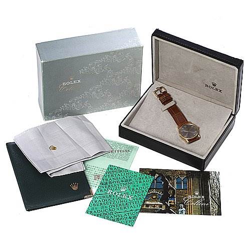 This image shows a Rolex Cellini 5116 Men's Yellow Gold Grey Dial 5116 Men's Yellow Gold Grey Dial watch from an angled top view, including its box, warranty card, manual, and polishing cloth.