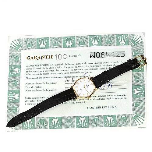 The image shows a Rolex Cellini 5112 Men's Yellow Gold White Dial 5112 Men's Yellow Gold White Dial watch laid flat, showcasing its face and black leather strap, placed on top of its certificate.