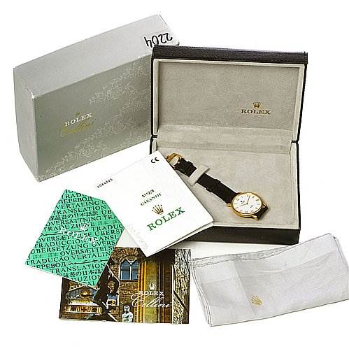 The image shows a Rolex Cellini 5112 Men's Yellow Gold White Dial 5112 Men's Yellow Gold White Dial watch at an angle, placed inside its box, accompanied by packaging, booklets, and a cleaning cloth.