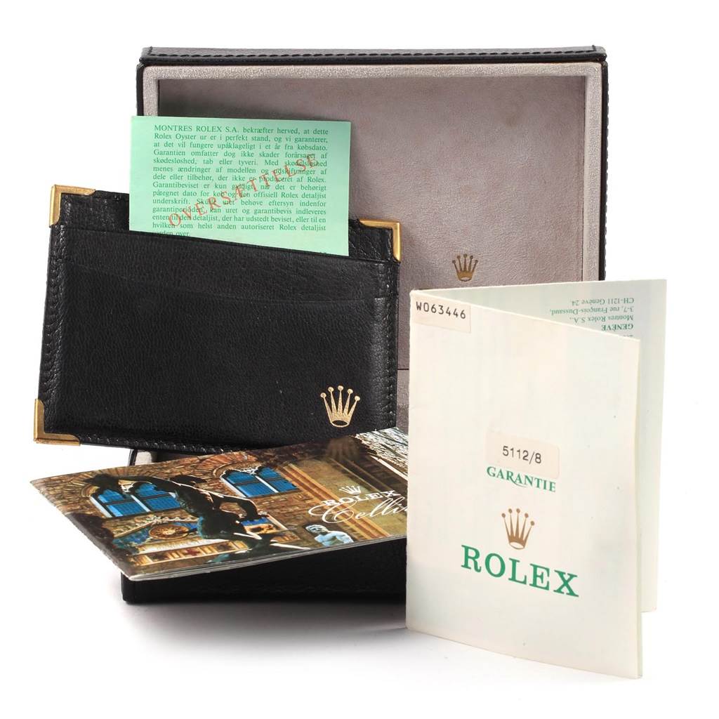 The image shows accessories and documentation for the Rolex Cellini 5112 Men's Yellow Gold Beige Dial 5112 Men's Yellow Gold Beige Dial, including guarantee booklets and a holder, with the box at the back.