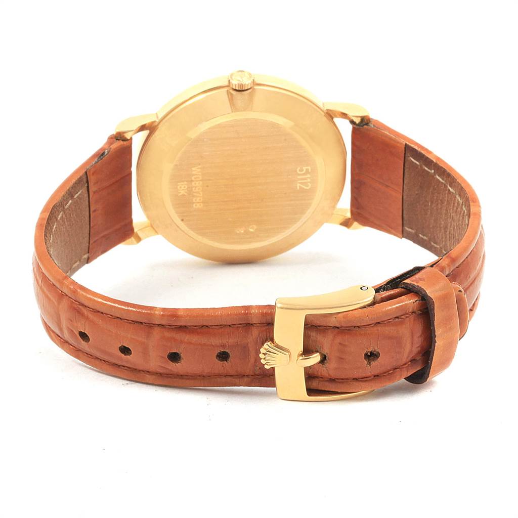 The image shows a rear view of a Rolex Cellini 5112 Men
s Yellow Gold Beige Dial 5112 Men
s Yellow Gold Beige Dial watch featuring its gold case back and brown leather strap with buckle.