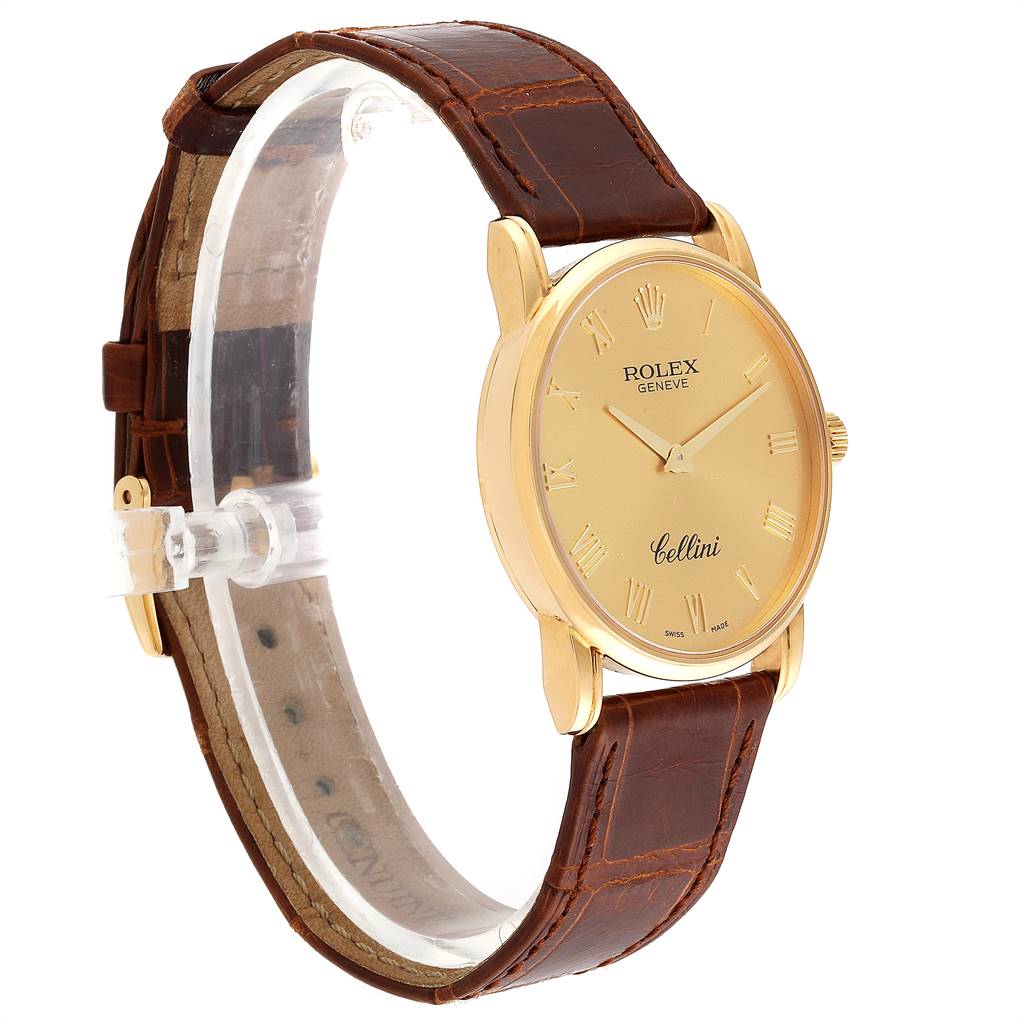 The Rolex Cellini 5116 Men's Yellow Gold Champagne Dial 5116 Men's Yellow Gold Champagne Dial watch is shown at a 3/4 angle, highlighting its gold case, brown leather strap, and clock face with Roman numeral markings.