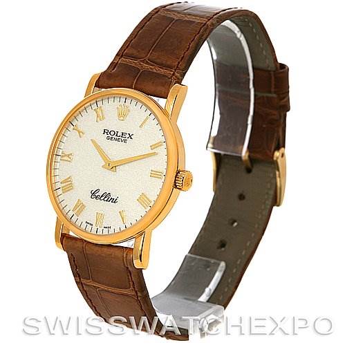 The Rolex Cellini 5115 Men's Yellow Gold Beige Dial 5115 Men's Yellow Gold Beige Dial watch is shown at a three-quarter angle, highlighting its gold case, brown leather strap, and face with Roman numerals.