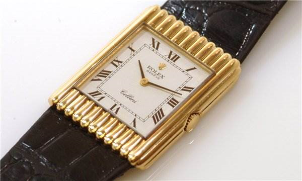 The image shows a top view of a Rolex Cellini model watch, highlighting its rectangular gold case, crown, white dial, and black leather strap.