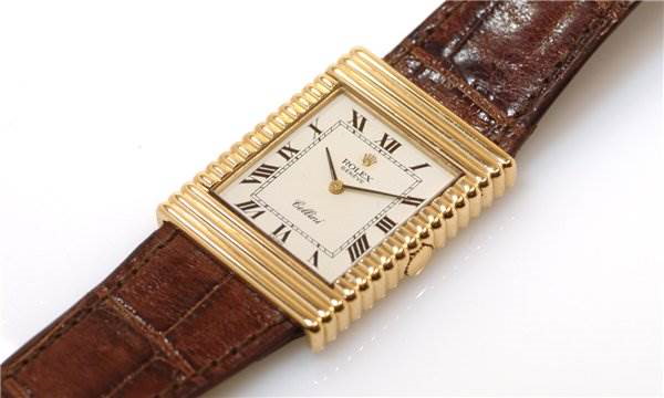 The Rolex Cellini watch is shown from an angled view, highlighting the rectangular face, gold case, and brown leather strap.