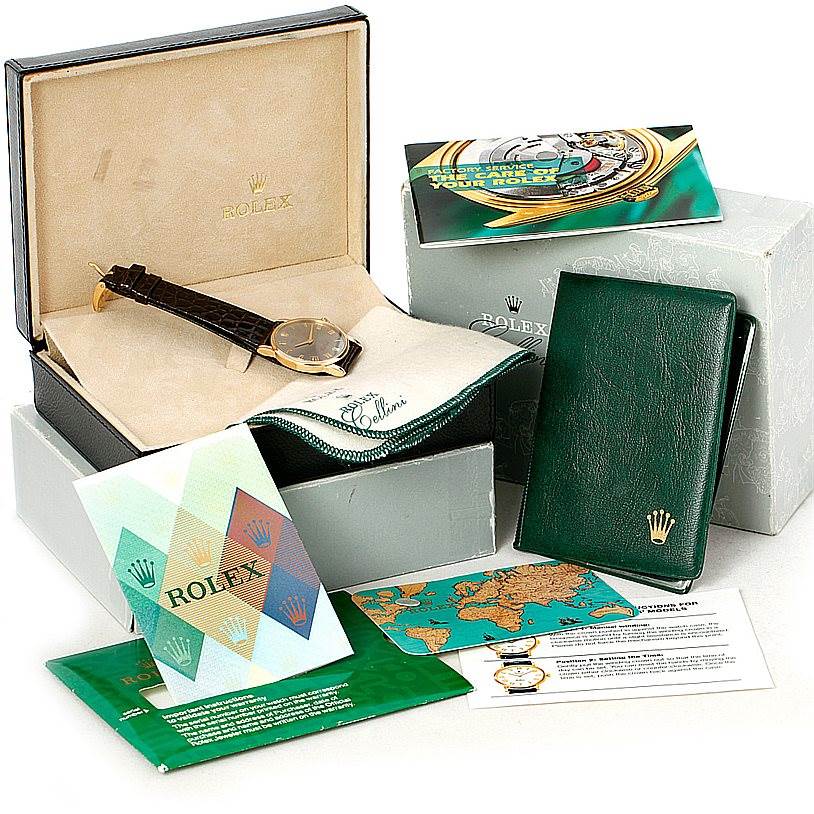 The Rolex Cellini 5116 Men's Yellow Gold Grey Dial 5116 Men's Yellow Gold Grey Dial watch is displayed in a box, accompanied by booklets, a pouch, and other packaging accessories.