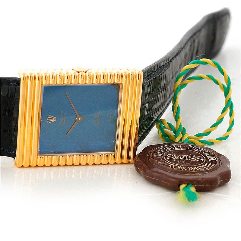 The image shows a close-up of a Rolex Cellini 4012 Men's Yellow Gold Blue Dial 4012 Men's Yellow Gold Blue Dial watch with a rectangular gold case, blue dial, black leather strap, and Swiss certification tag.