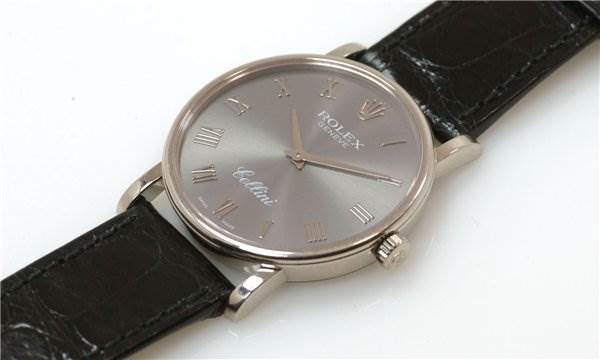 The image shows a Rolex Cellini 5115/9 Men
s White Gold Grey Dial 5115/9 Men
s White Gold Grey Dial watch from a slight side angle, displaying its face, crown, and black leather strap.