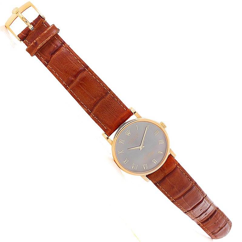 The Rolex Cellini 5115 Men's Yellow Gold Grey Dial 5115 Men's Yellow Gold Grey Dial watch is shown from a top-down angle, displaying its brown leather strap, gold case, and dial with Roman numerals.