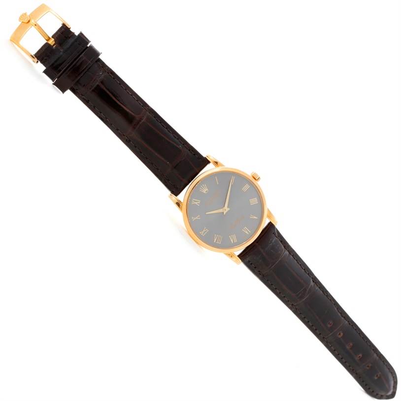 The Rolex Cellini 5116 Men's Yellow Gold Grey Dial 5116 Men's Yellow Gold Grey Dial watch is shown from a top-down angle, featuring its face, black leather strap, and gold buckle.