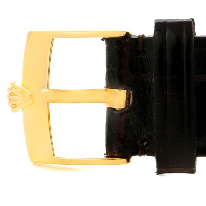 The image shows a close-up of a Rolex Cellini 5116 Men
s Yellow Gold Champagne Dial 5116 Men
s Yellow Gold Champagne Dial watch
s gold buckle and a portion of its dark leather strap.