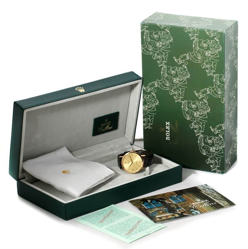 The image shows a Rolex Cellini 4112 Men
s Yellow Gold Champagne Dial 4112 Men
s Yellow Gold Champagne Dial watch, its open box, an outer green box, a cloth, and some documents.
