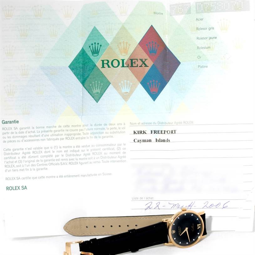 The image shows a Rolex Cellini 5115 Men
s Yellow Gold Black Dial 5115 Men
s Yellow Gold Black Dial watch laying flat next to its warranty document.
