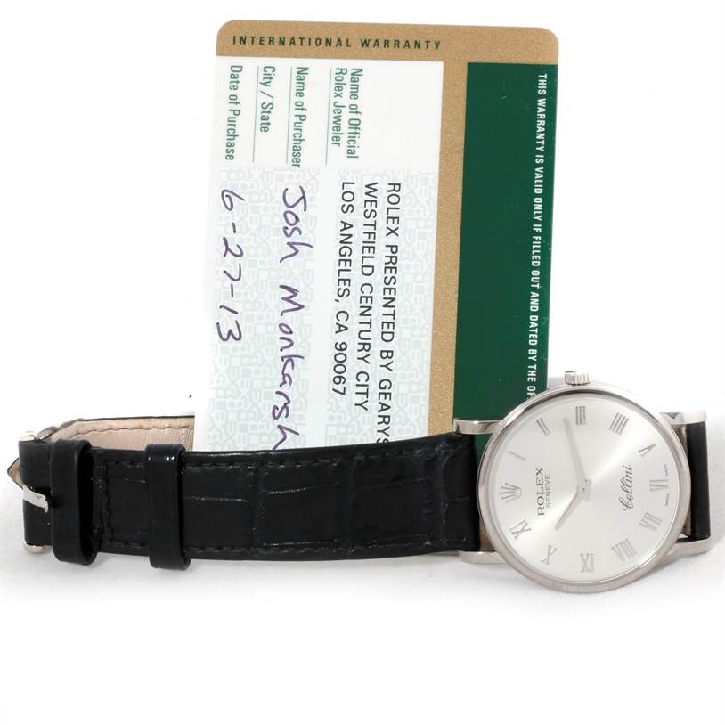 The image shows a Rolex Cellini 5115 Men
s White Gold Silver Dial 5115 Men
s White Gold Silver Dial model watch with a black leather strap, positioned horizontally alongside its international warranty card.
