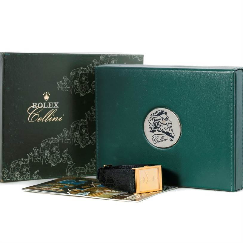 The image shows packaging and a Rectangular gold-faced Rolex Cellini 5071 Men's Yellow Gold Champagne Dial 5071 Men's Yellow Gold Champagne Dial watch with a black band, along with its box and booklet.