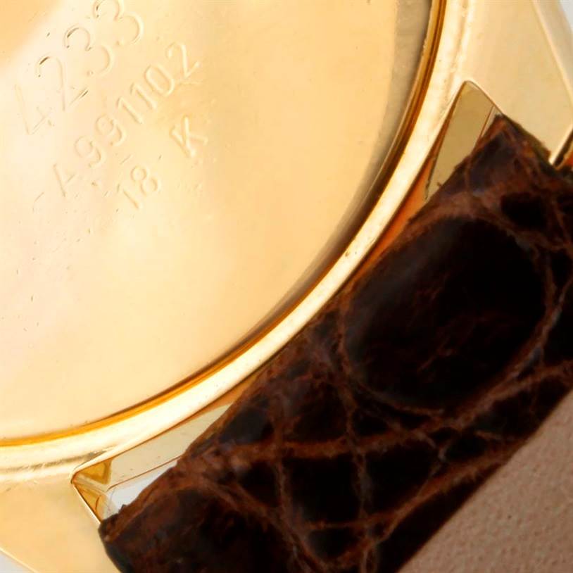 The image shows the back case of a Rolex Cellini 4233 Men
s Yellow Gold White Dial 4233 Men
s Yellow Gold White Dial watch with a focus on its 18k gold marking and a part of the leather strap.