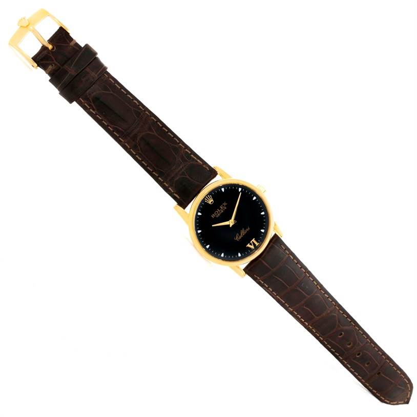 The image shows a top view of a Rolex Cellini 5116 Men
s Yellow Gold Black Dial 5116 Men
s Yellow Gold Black Dial watch with a black dial, gold case, and brown leather strap.