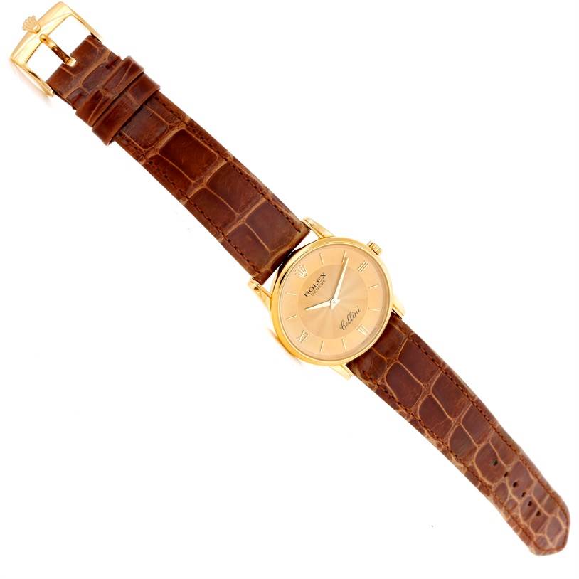 The image shows a top-down angle of a Rolex Cellini 5116 Men
s Yellow Gold Champagne Dial 5116 Men
s Yellow Gold Champagne Dial watch, displaying its brown leather strap and golden watch face.