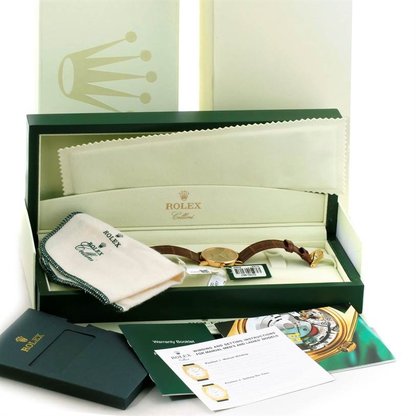 The image shows a Rolex Cellini 5115 Men
s Yellow Gold Champagne Dial 5115 Men
s Yellow Gold Champagne Dial watch, its box, a cloth, and warranty booklets, all at a slightly elevated angle.