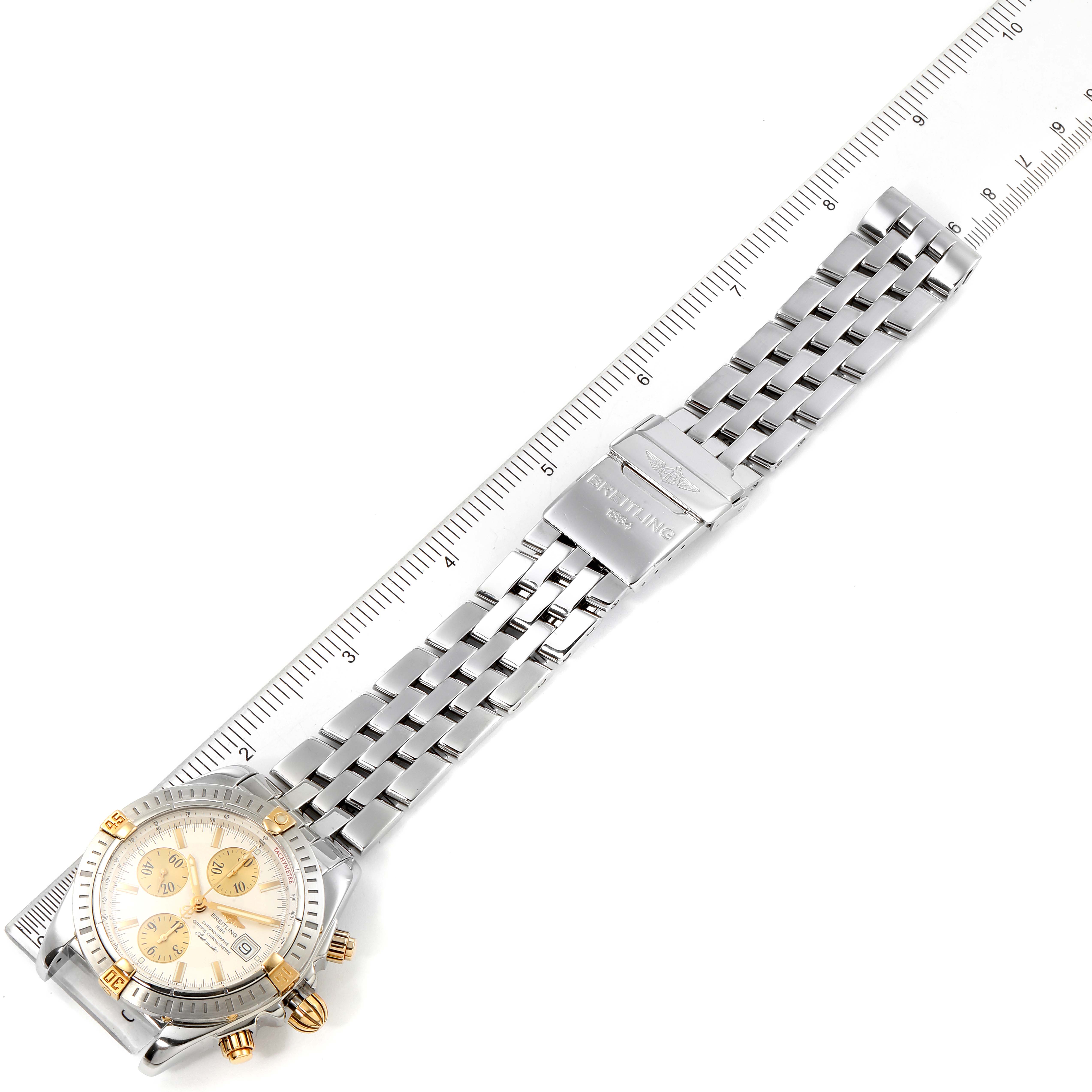 The image shows a top-down view of a Breitling Chronomat B13356 Men
s Stainless Steel Silver Dial B13356 Men
s Stainless Steel Silver Dial watch and metal bracelet, next to a ruler.