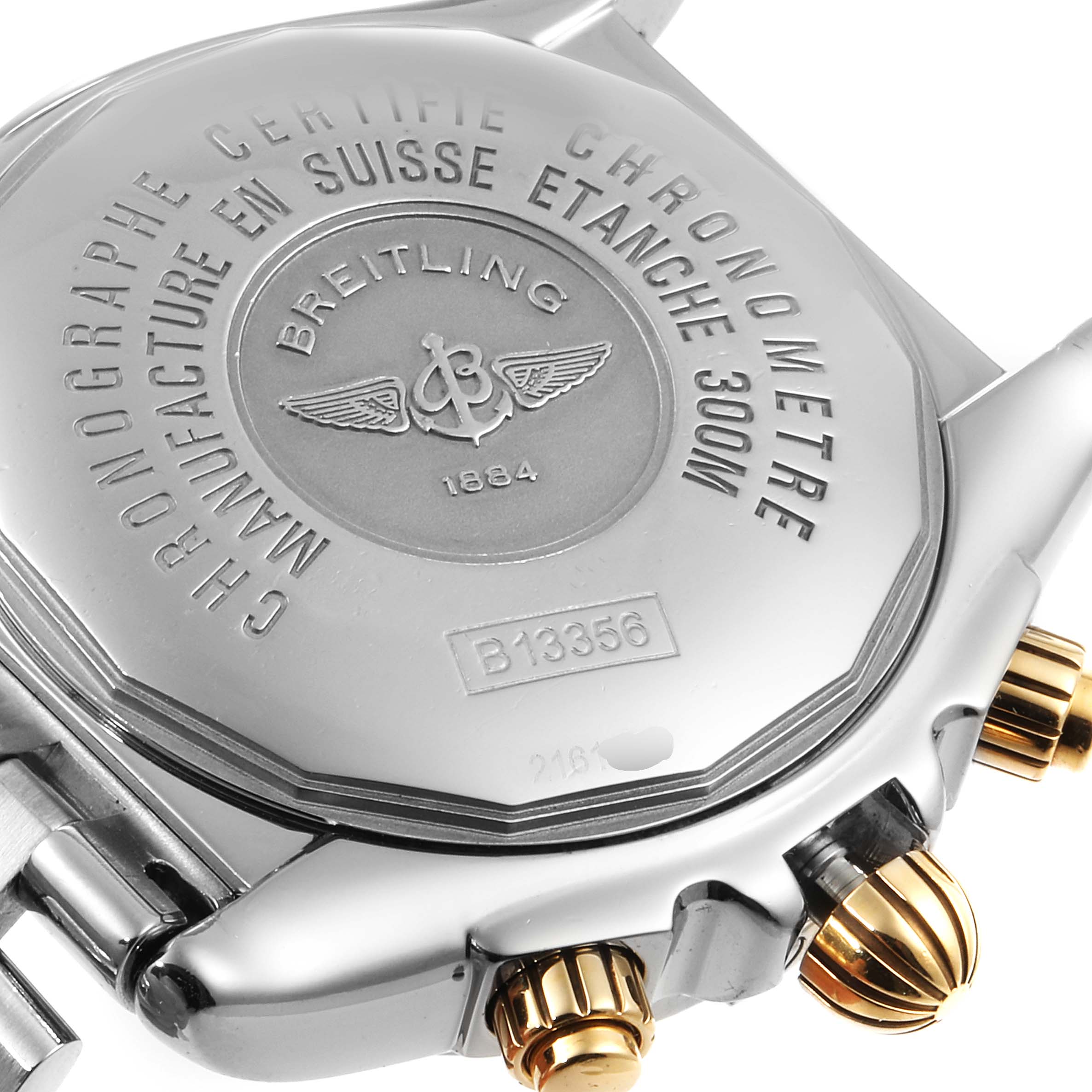 The image shows the case back and crown of a Breitling Chronomat B13356 Men
s Stainless Steel Silver Dial B13356 Men
s Stainless Steel Silver Dial watch, emphasizing its engravings and gold accents.