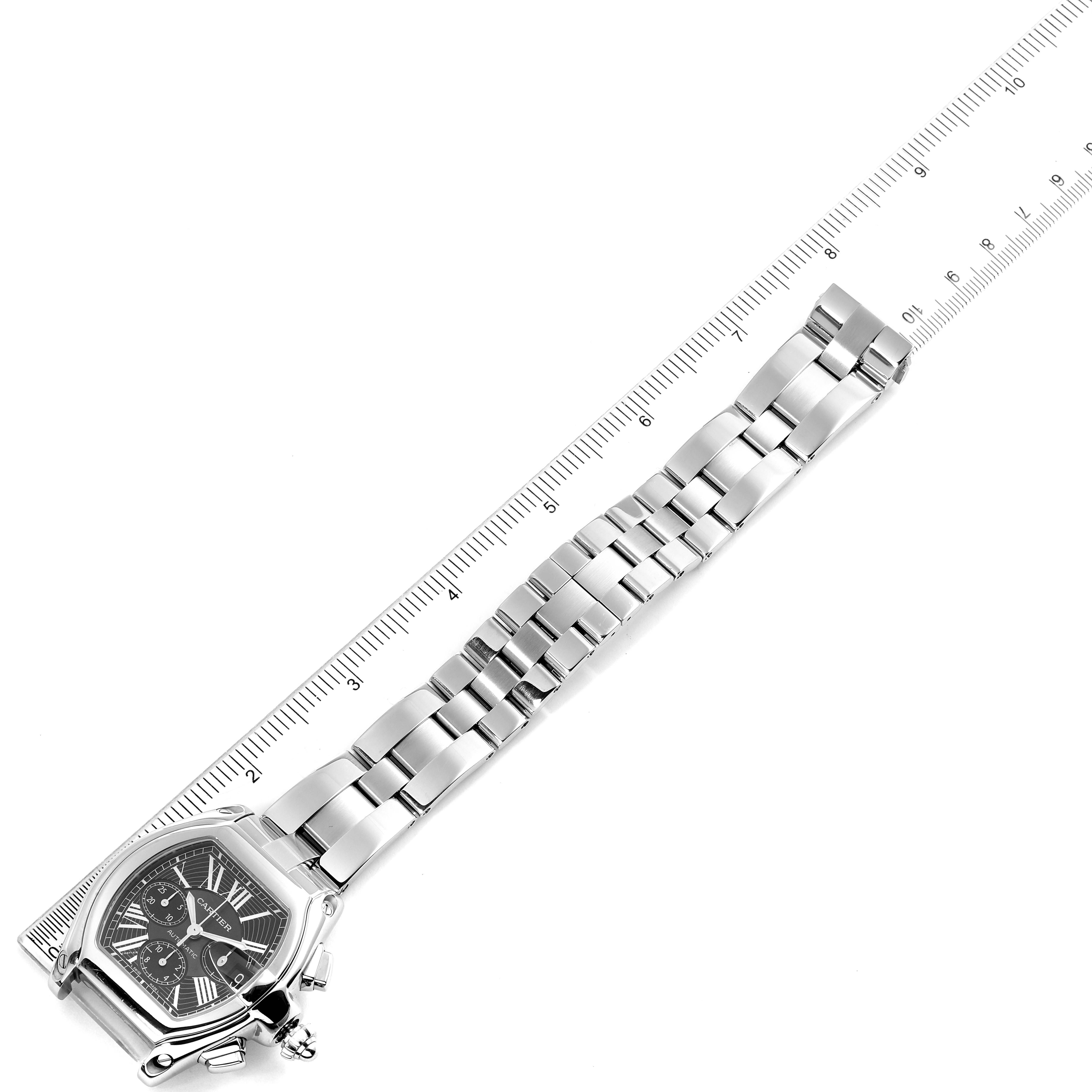 The image shows a Cartier Roadster W62020X6 Men
s Stainless Steel Black Dial W62020X6 Men
s Stainless Steel Black Dial watch positioned next to a ruler, highlighting its stainless steel bracelet and face.
