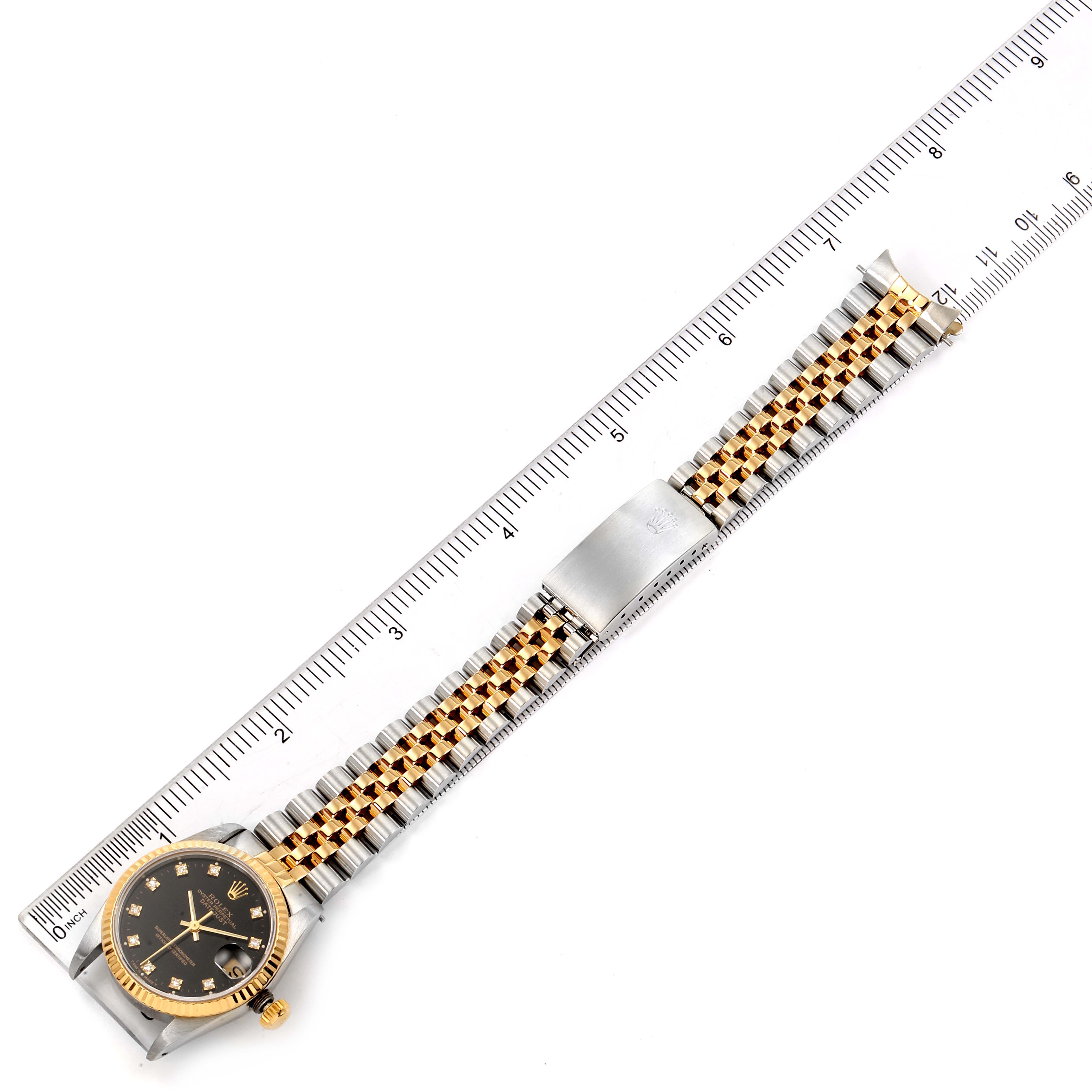 The image shows a top-down view of a Rolex Mid-Size 68273 Women
s Steel and Gold (two tone) Black Dial 68273 Women
s Steel and Gold (two tone) Black Dial watch with a ruler for scale, highlighting the bracelet and watch face.