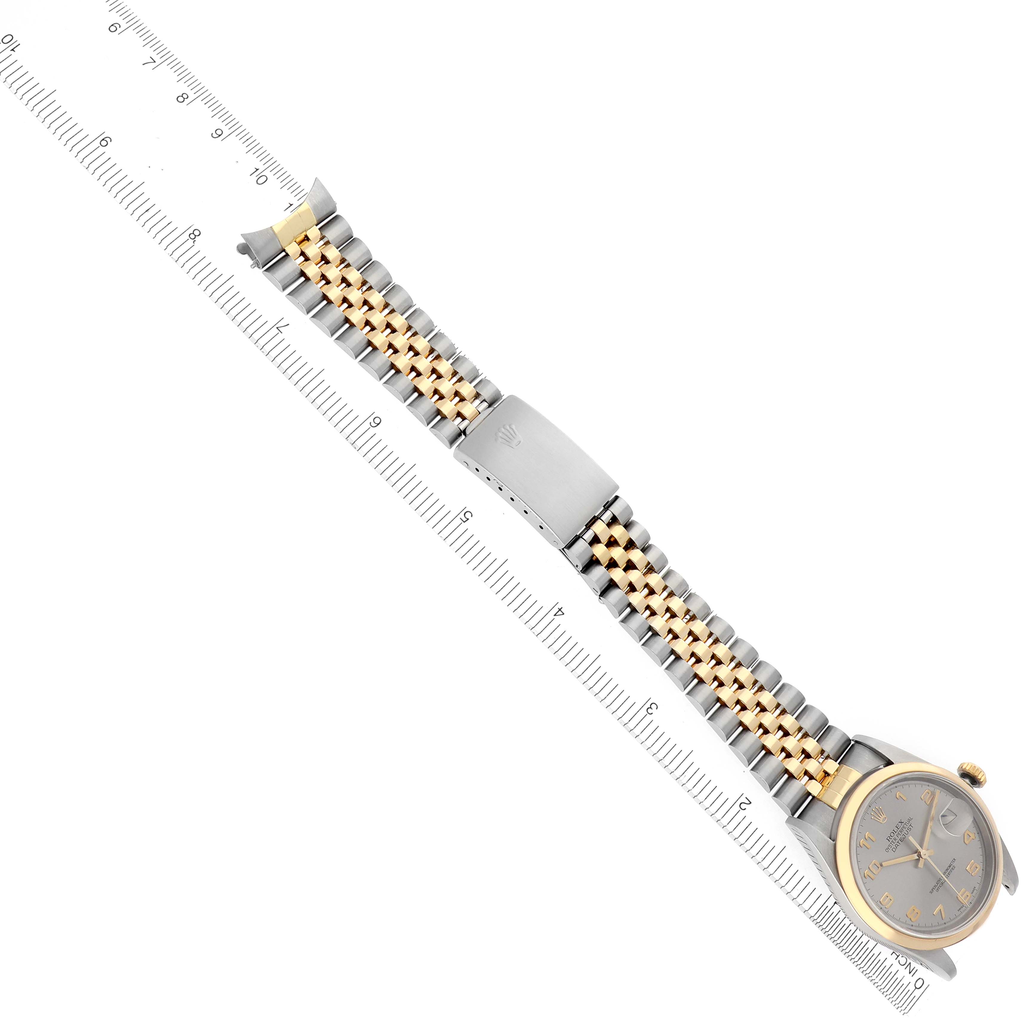 The Rolex Datejust 16203 Men's Steel and Gold (two tone) Grey Dial 16203 Men's Steel and Gold (two tone) Grey Dial watch is shown at an angled top view, displaying the face, bracelet, and clasp beside a ruler.