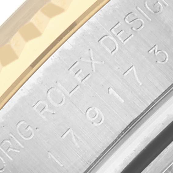 This close-up image of a Rolex Datejust 179173 Women's Steel and Gold (two tone) White Dial 179173 Women's Steel and Gold (two tone) White Dial watch shows part of the bezel with engraved text.