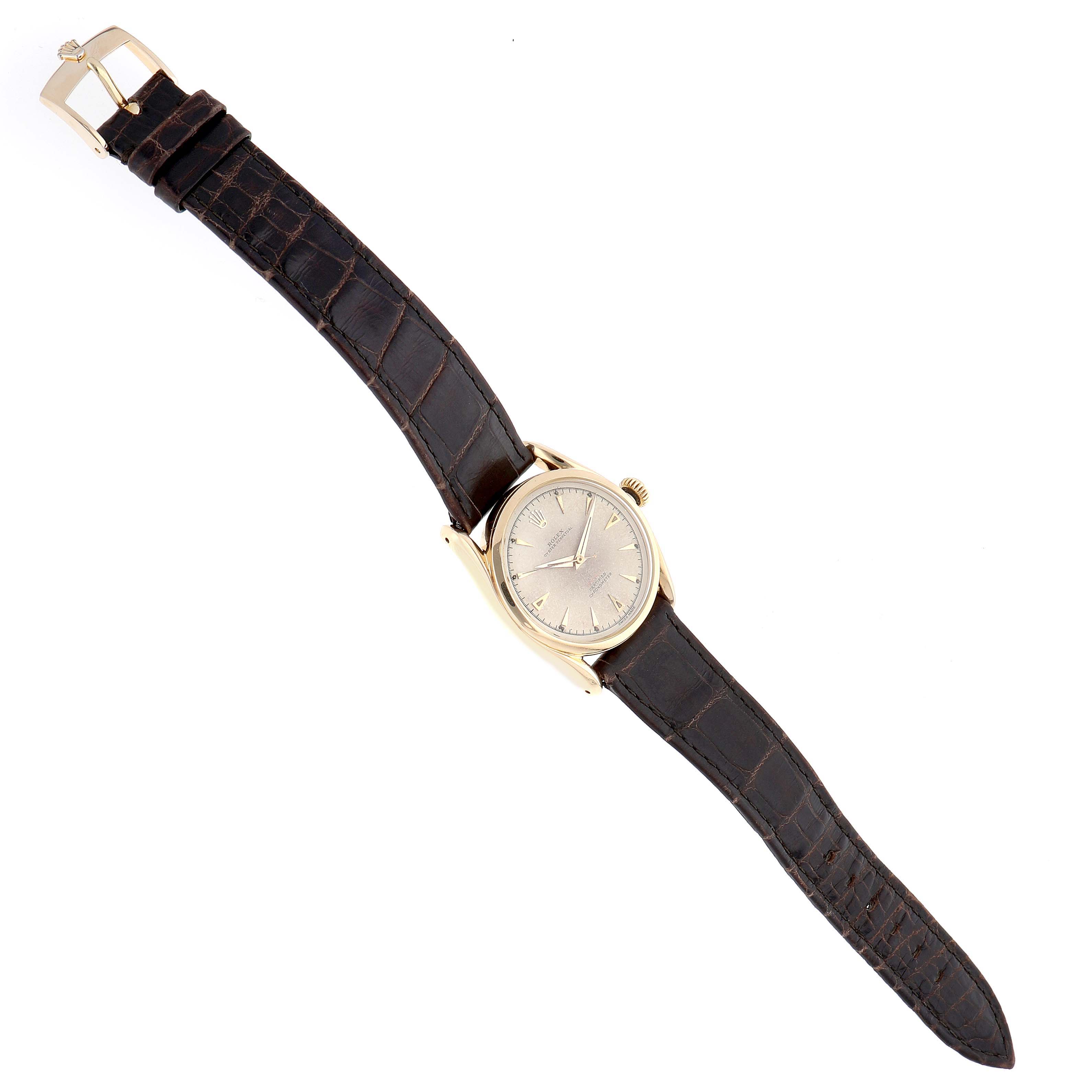 The Rolex Oyster Perpetual 6085 Men's Yellow Gold Champagne Dial watch is shown from a top-down angle, highlighting the dial, case, and leather strap.