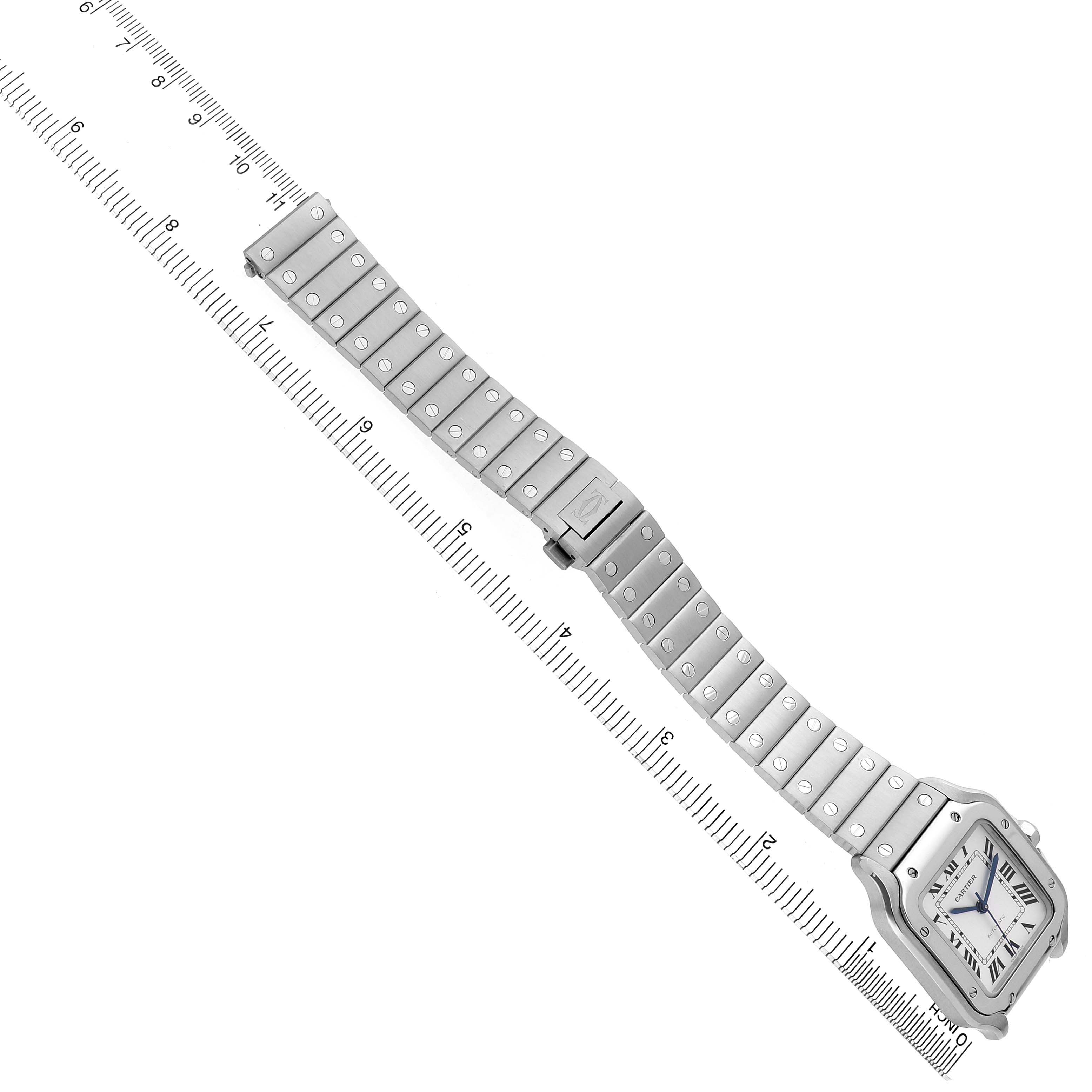 The image shows a top-down view of a Cartier Santos WSSA0029 Men's Stainless Steel Silver Dial watch, highlighting the bracelet and face with a measuring ruler.