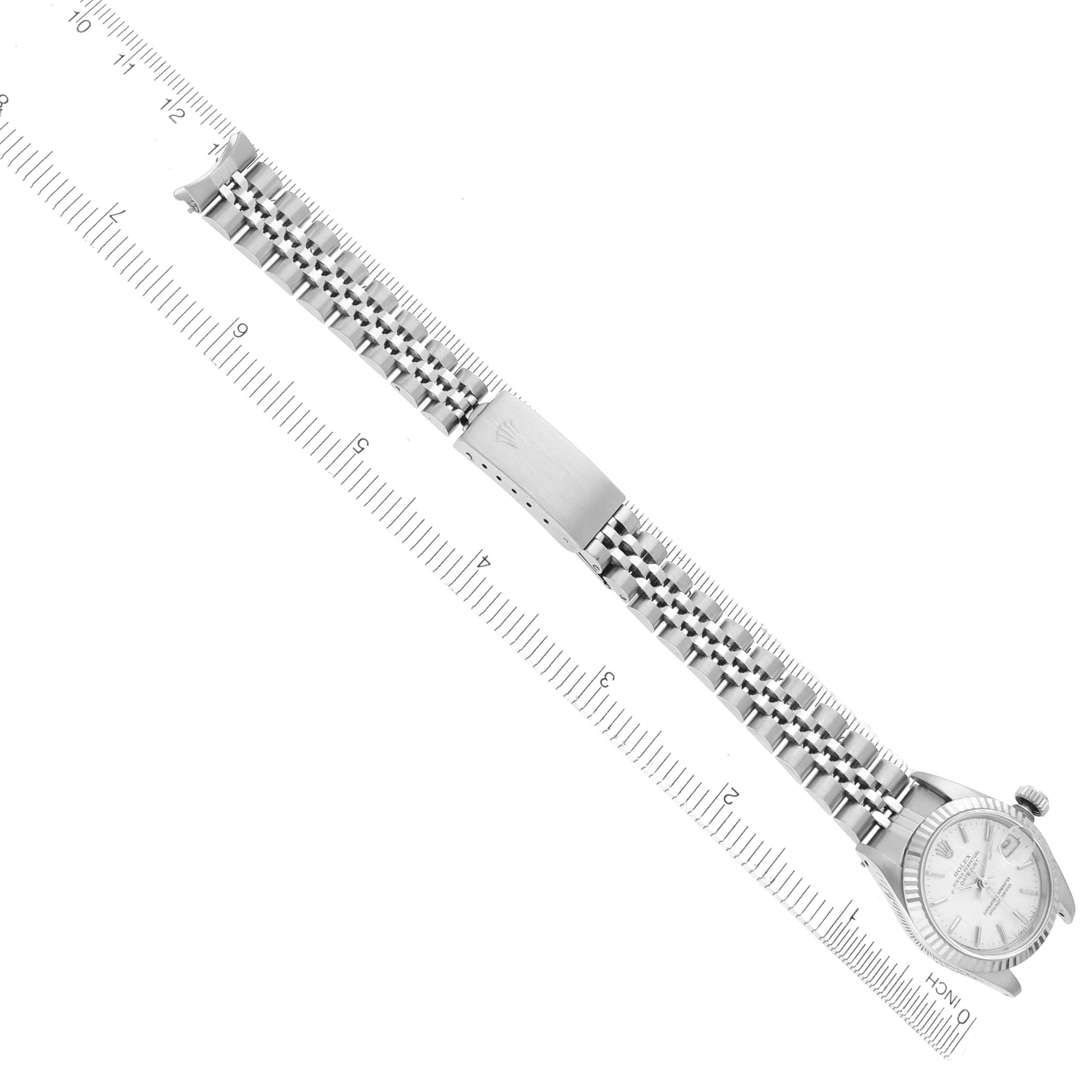 The Rolex Date 69174 Women's Stainless Steel Silver Dial 69174 Women's Stainless Steel Silver Dial model watch is shown at a diagonal angle, detailing the watch face and bracelet with a clasp alongside a ruler.